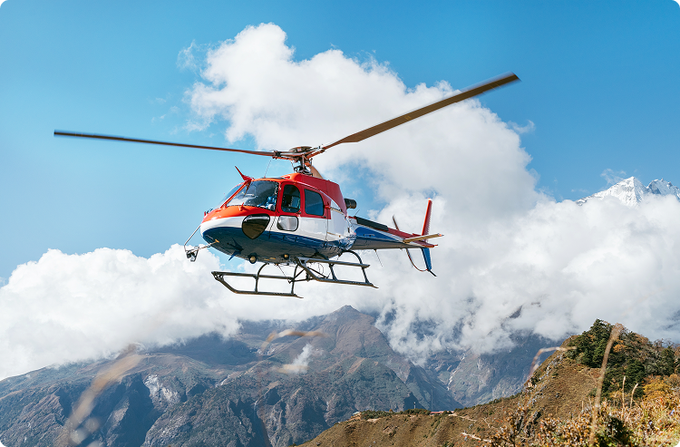 A rescue helicopter flies in front of mountains that reach through the clouds