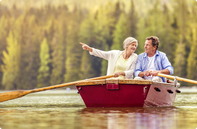 A Senior couple rows in a small rowboat in an alpine lake. The woman signals for her husband to look at something in the distance