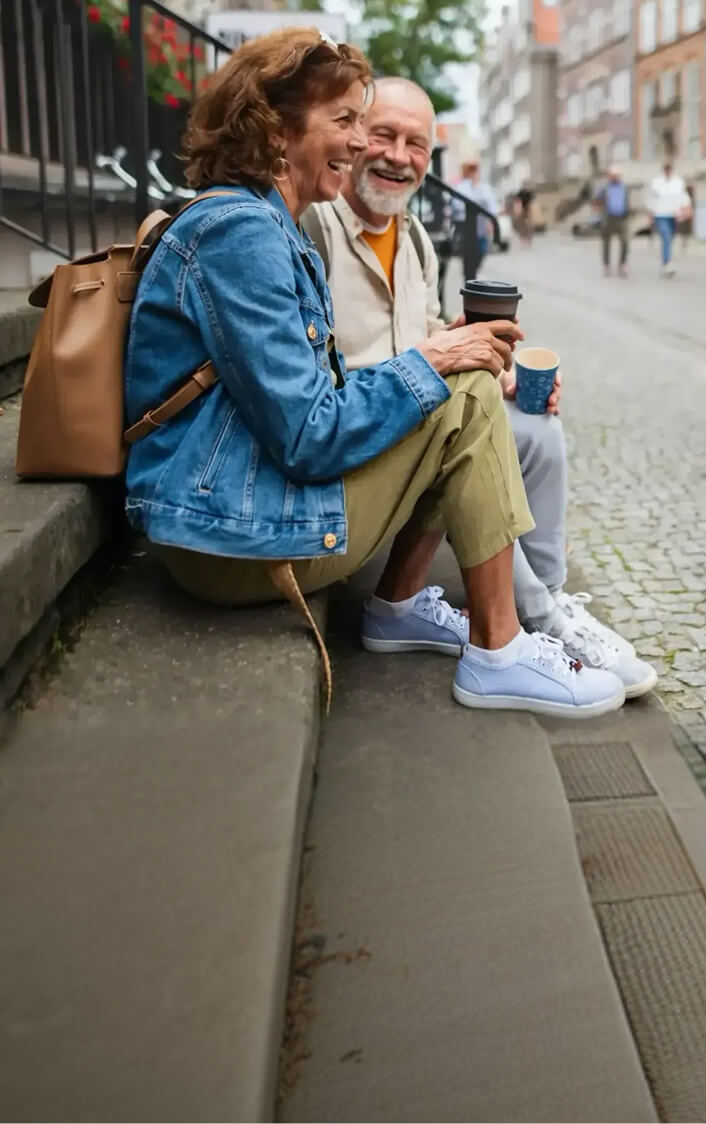 An older couple sitting on the steps of a building while holding coffee cups.